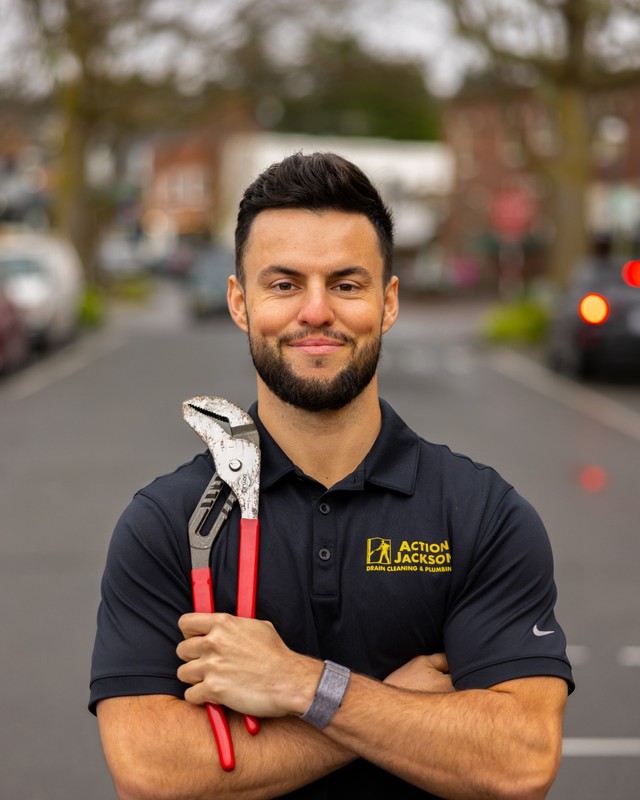 Isaac Jackson of Action Jackson Plumbing standing in a residential street holding a pipe wrench