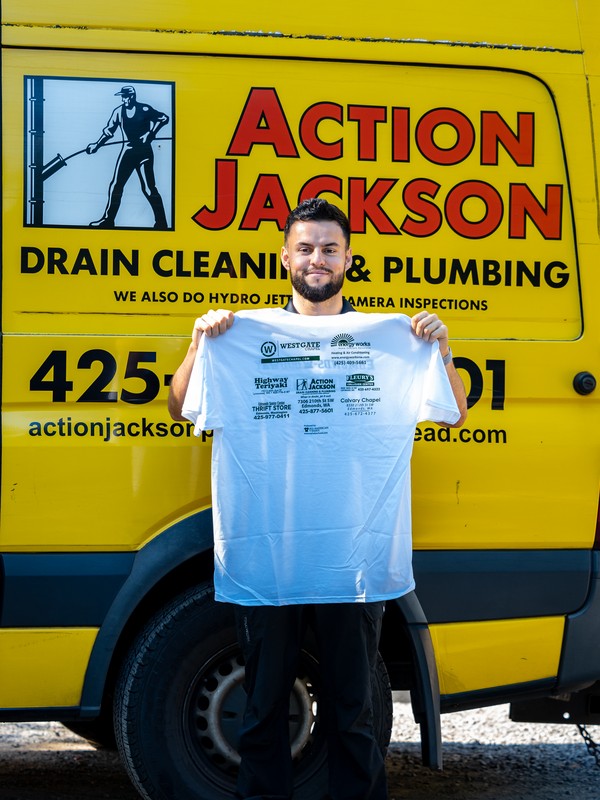 Isaac Jackson in front of the yellow Action Jackson van, holding a community sponsor shirt
