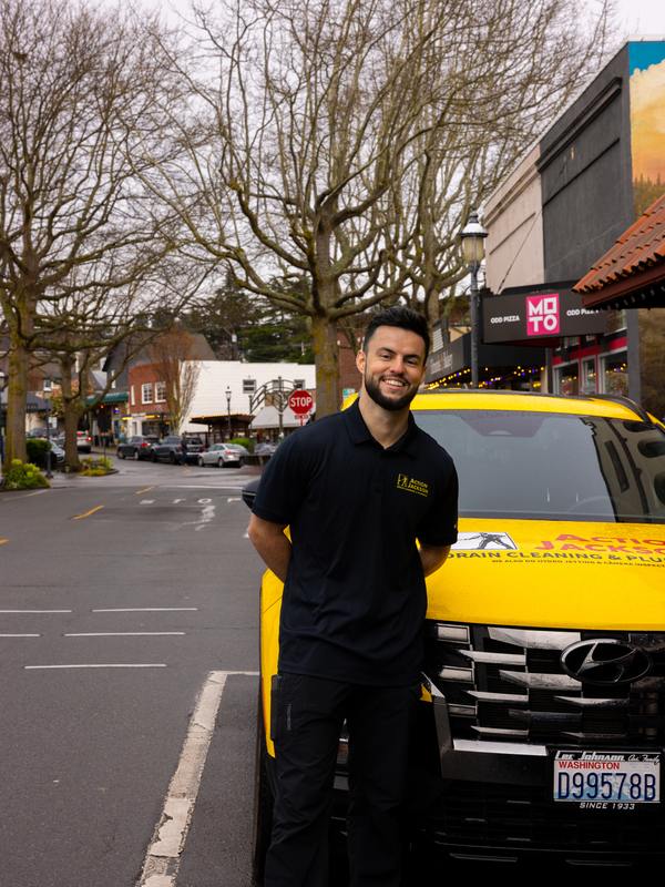 Isaac Jackson standing beside a yellow Action Jackson Plumbing vehicle on a street in downtown Edmonds