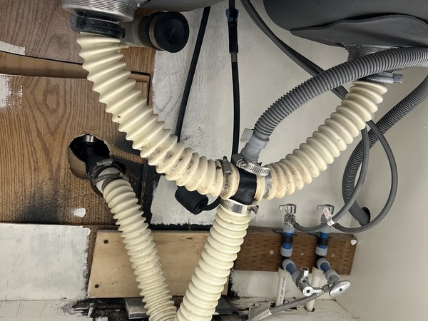 Corrugated drain hoses under a kitchen sink with water damage on the cabinet floor